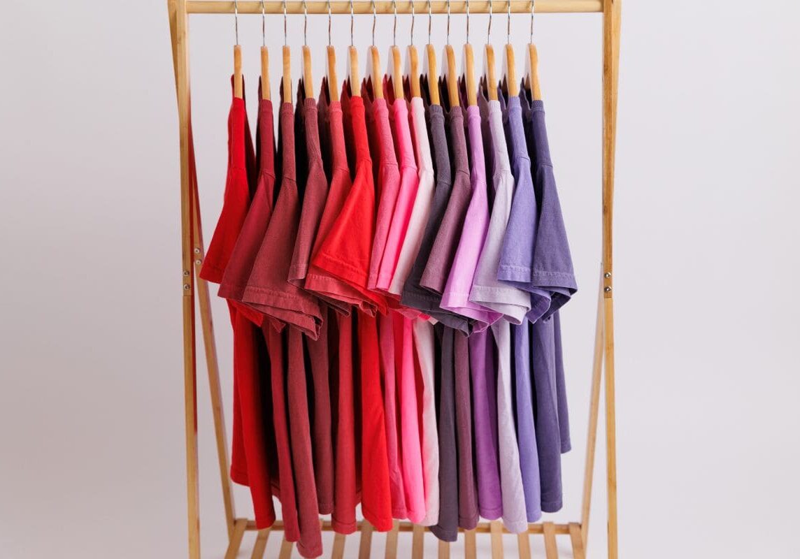 Colorful t-shirts hanging on wooden rack.
